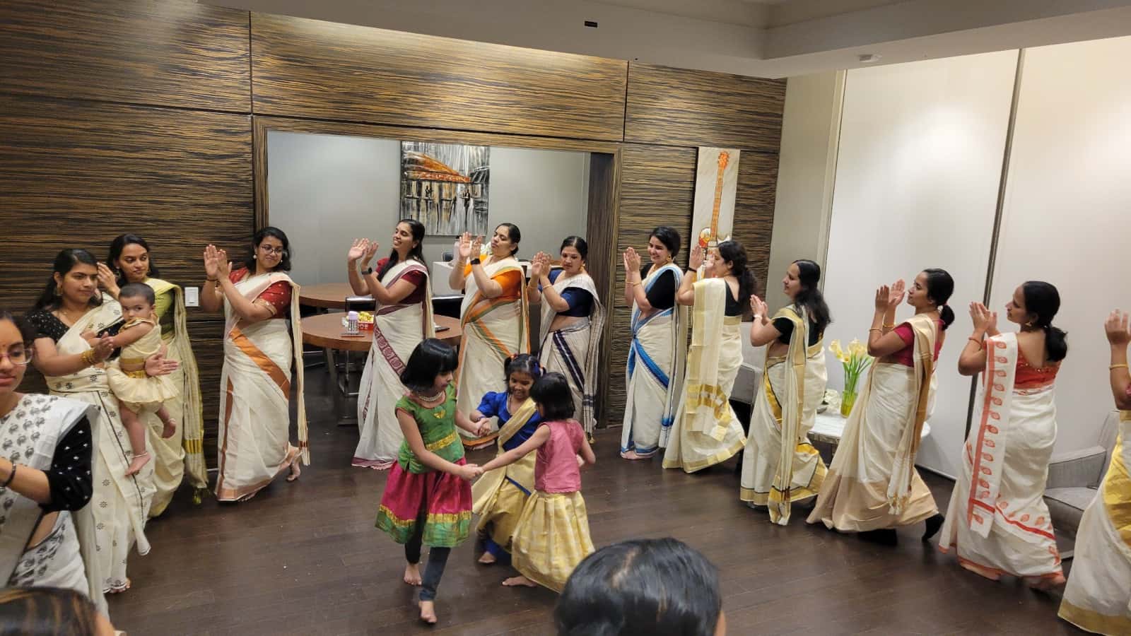 Women in kasavu saris clapping in a Thiruvathira circle while three young girls hold hands and dance in the middle